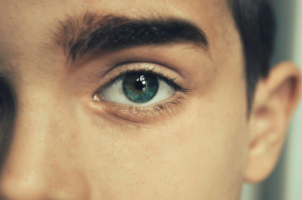 A detailed close-up photo of a young man's blue eye, highlighting texture and color.