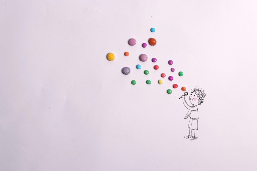 Creative drawing of a child blowing colorful candy bubbles on white background.
